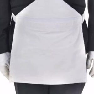 May include: A white apron with a bib and waist tie, worn over a black suit. The apron is rectangular with a triangular bib. The person is wearing white gloves. This apron is suitable for service industry professionals.