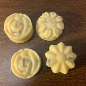 May include: Four small, round, white soap bars with different designs. The designs are a rose, a sunflower, a star, and another rose.