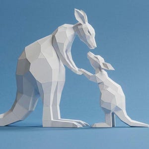 Puede incluir: Una escultura de papel blanco de un canguro y su cría sobre un fondo azul. El canguro adulto extiende la mano para tocar la del pequeño. La escultura tiene un diseño geométrico poligonal.