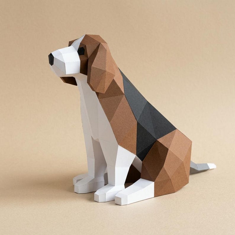 Op de afbeelding: Een geometrische papieren sculptuur van een beagle-hond in zittende positie. De hond heeft een wit, bruin en zwart kleurenschema, met een polygonale vormgeving. De sculptuur staat tegen een neutrale achtergrond.