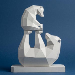 May include: A white paper sculpture of two polar bears. One bear is standing upright, supporting another bear on its back. The bears are made of geometric shapes and are on a rectangular base. The background is a solid blue.