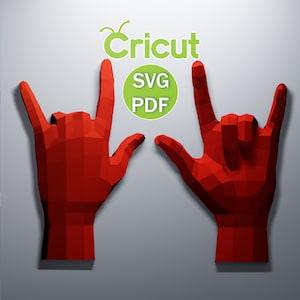 Puede incluir: Dos manos de papel rojas, tridimensionales, haciendo el gesto de rock and roll. Las manos están sobre un fondo gris. El texto "Cricut" y "SVG PDF" es visible en la imagen.