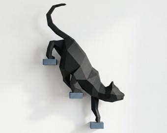 Könnte beinhalten: Eine schwarze, geometrische Katzenskulptur, die drei graue Stufen hinabsteigt. Der Körper der Katze besteht aus eckigen Formen, was eine moderne, minimalistische Ästhetik erzeugt. Die Skulptur ist an einer weißen Wand befestigt.