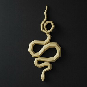 May include: A geometric, golden-colored snake sculpture against a black background. The snake is stylized with angular segments, creating a modern, artistic aesthetic. The sculpture is a decorative wall hanging.