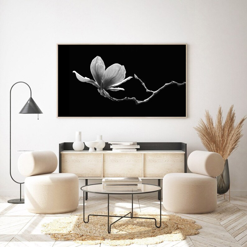 May include: A black and white photograph of a single magnolia flower in bloom against a black background. The flower is in focus, while the branch it is on is slightly out of focus.