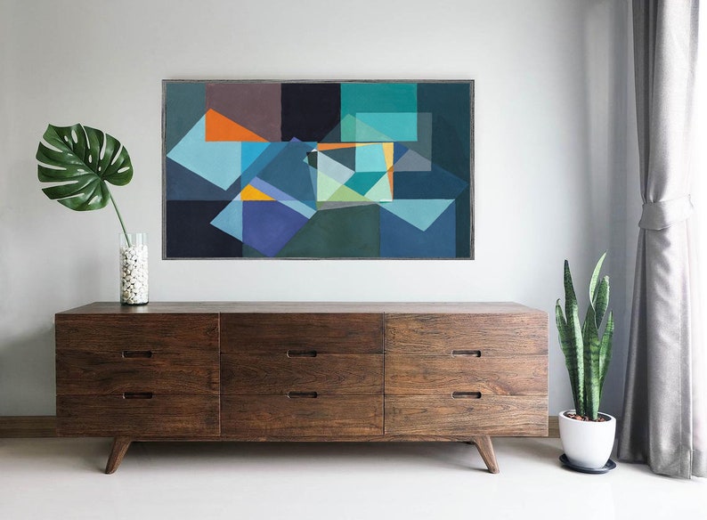 May include: Abstract geometric painting with blue, orange, and green shapes. The artwork hangs above a mid-century modern wooden dresser. A monstera leaf in a vase and a potted snake plant add to the decor.