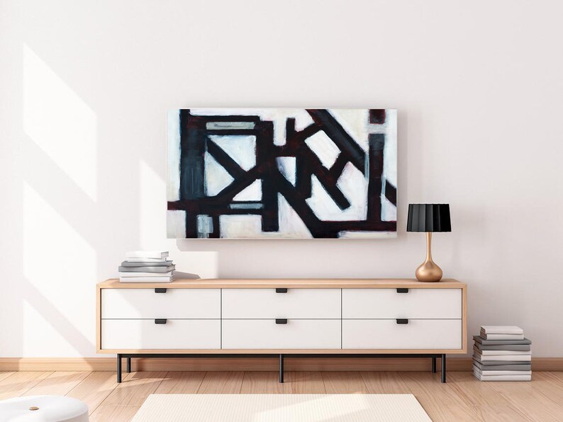 May include: A white dresser with six drawers and black handles sits on a wooden floor. A black and white abstract painting hangs above the dresser. A gold lamp with a black shade sits on the right side of the dresser.