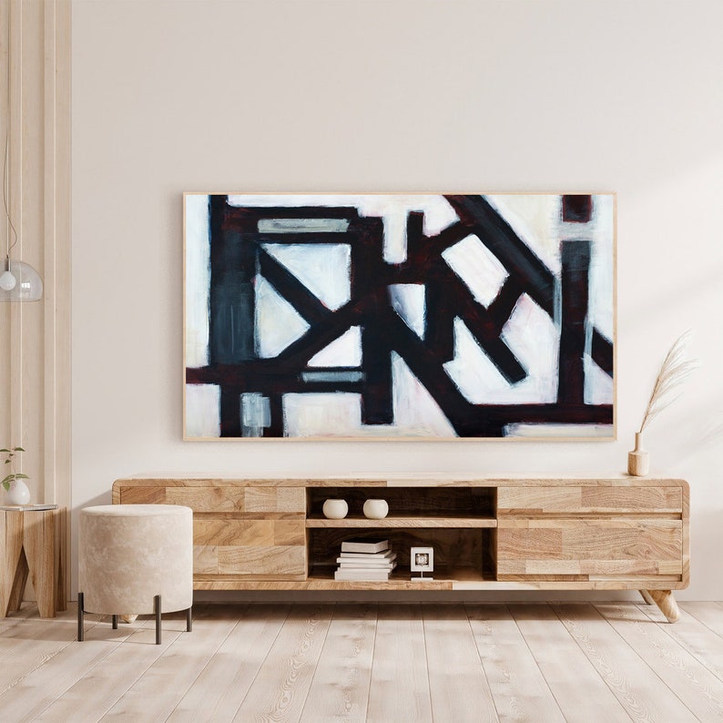 May include: Abstract painting with black, white, and gray geometric shapes on a white background. The painting is framed in a natural wood frame and is hanging on a white wall above a wooden media console.