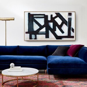May include: A blue velvet sectional sofa with a black and white abstract painting above it. The sofa has two throw pillows, one black and one burgundy. A gold floor lamp is on the left side of the sofa. A round marble coffee table sits in front of the sofa.