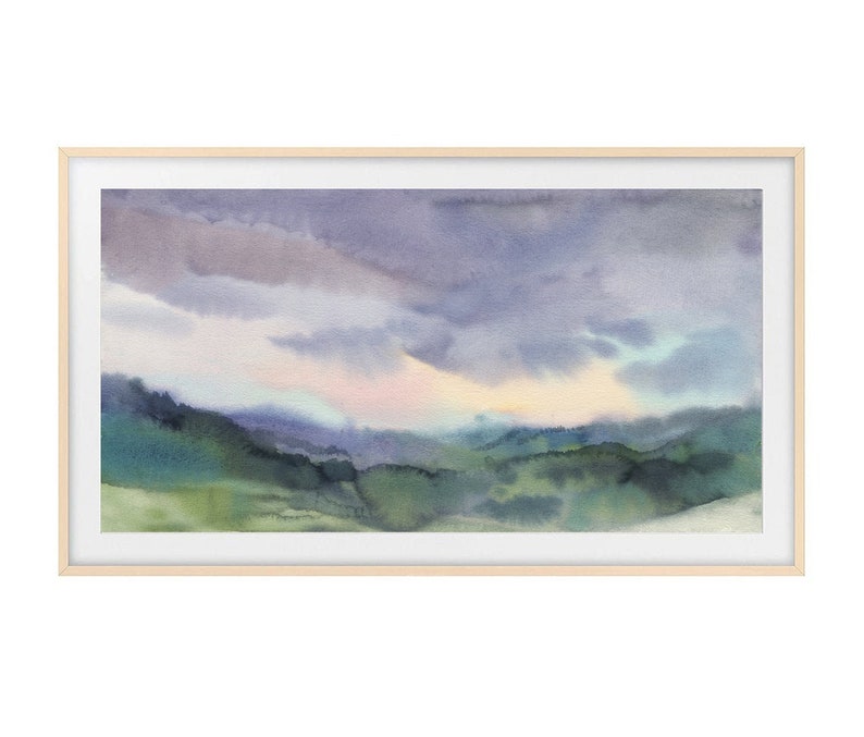 May include: Watercolor landscape painting featuring a serene mountain scene under a cloudy sky. The artwork showcases shades of green, blue, and purple, framed in a light wood frame. The painting evokes a sense of tranquility.