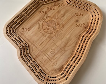 May include: Wooden cribbage board shaped like Fenway Park, the home of the Boston Red Sox. The board has a baseball diamond in the center and numbers around the perimeter, including 310, 379, 389, 420, 380, and 302.