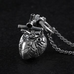 Op de afbeelding: Een zilveren anatomisch hart hanger ketting met een gedetailleerd, getextureerd ontwerp. Het hart is bevestigd aan een zilveren ketting.