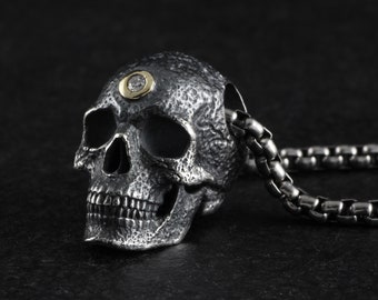 May include: A silver skull pendant with a textured surface and a small diamond set in a gold bezel on the forehead. The pendant is attached to a silver chain.