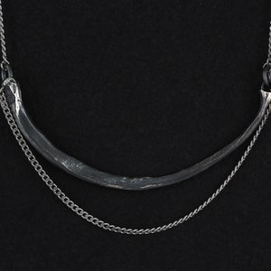 May include: A silver necklace with a curved, textured pendant and a delicate chain.