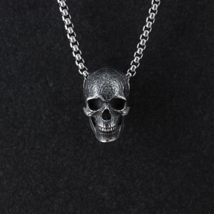 May include: A silver skull pendant necklace on a black background.