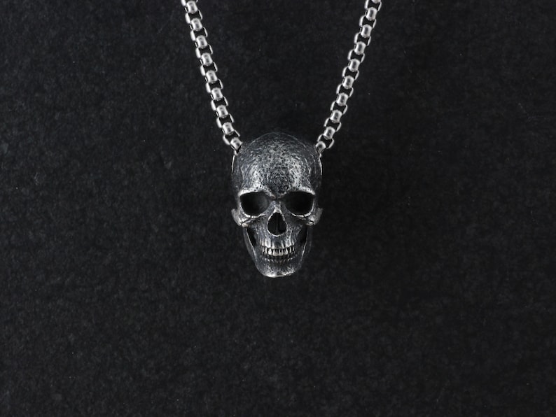May include: A silver skull pendant necklace on a black background.
