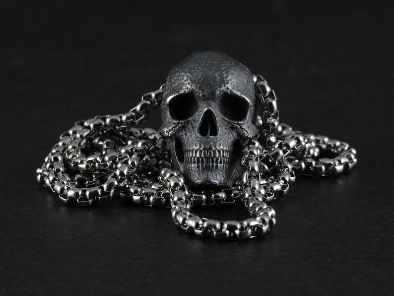 May include: A silver skull pendant on a silver chain. The skull has a detailed design and is a popular gothic style accessory.