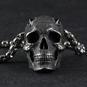 May include: A silver skull pendant with red gemstone eyes and horns, attached to a silver chain.