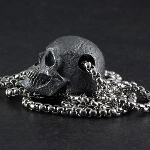 May include: A silver chain necklace with a detailed skull pendant. The skull is made of a dark metal and has a realistic design.