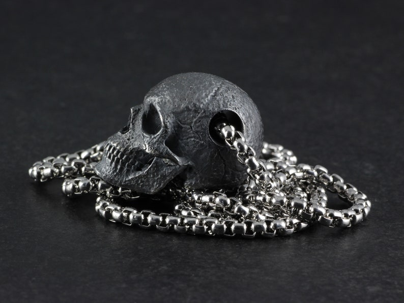 May include: A silver chain necklace with a detailed skull pendant. The skull is made of a dark metal and has a realistic design.