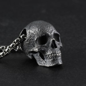 May include: A silver skull pendant necklace with a detailed, textured design. The skull has a chain link necklace.