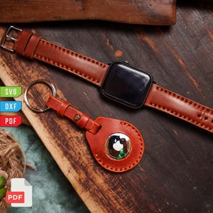 Pu&ograve; includere: Un cinturino in pelle marrone e uno smartwatch nero sono esposti accanto a un portachiavi in pelle marrone abbinato con un anello argentato. Il portachiavi contiene un Apple AirTag argentato. Gli oggetti sono su una superficie di legno.