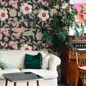 May include: A white couch with green velvet pillows sits in front of a floral wallpaper with a black background. A small black coffee table with wooden legs sits in front of the couch. A white rug is on the floor.