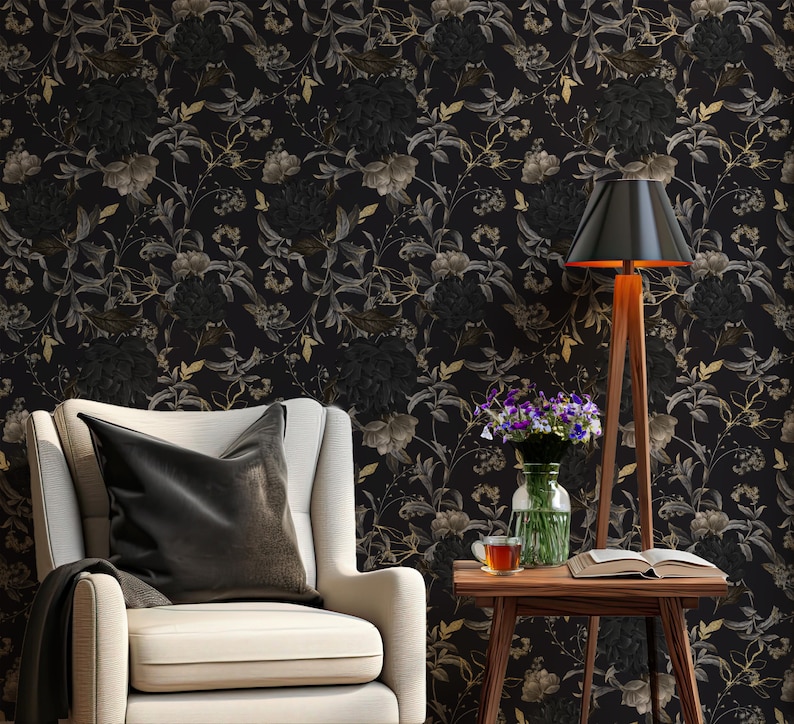 K&ouml;nnte beinhalten: Ein wei&szlig;er Sessel mit einem schwarzen Kissen steht vor einer schwarzen Tapeten mit Blumenmuster. Neben einem kleinen Holztisch mit einem Buch, einer Tasse und einer Vase mit lila Blumen steht eine schwarze Lampe mit einem Holzstativ.