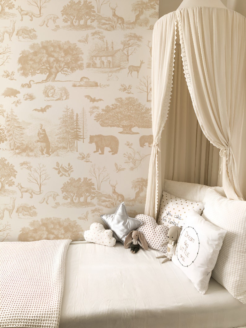 May include: A cozy nursery scene featuring a cream-colored canopy bed with decorative pillows and a white waffle-knit blanket. The wallpaper has a beige forest scene design. Plush toys include a star, cloud, and heart-shaped pillow.