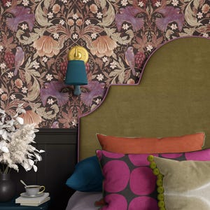 May include: A bedroom interior with patterned wallpaper depicting birds and flowers. The room features a green headboard, vibrant cushions, and a teal bedside table with a vase and a cup of tea. A teal wall lamp is mounted on the wall.