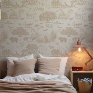 May include: A bedroom scene featuring a bed with white linens and tan pillows, complemented by a matching throw. The wall is adorned with wallpaper depicting a forest scene with bears, deer, and trees. A pink lamp and a woven basket add decorative touches.
