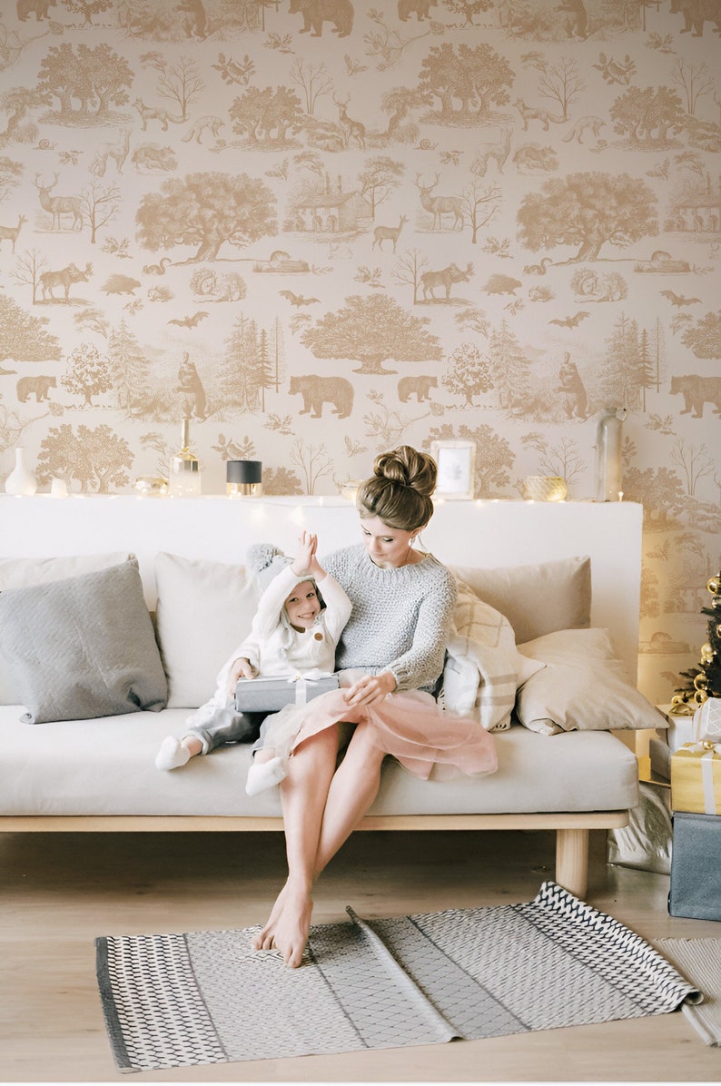 May include: A woman and child are seated on a light-colored sofa, with a gift box. The background features a beige wallpaper with a forest scene. A gray and white patterned rug is on the floor.