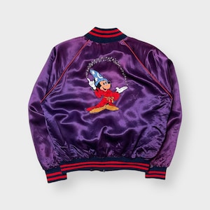 May include: A purple satin jacket with a red and navy blue striped collar, cuffs, and hem. The back features an embroidered image of Mickey Mouse in a wizard costume, surrounded by stars. Red piping accents the seams.