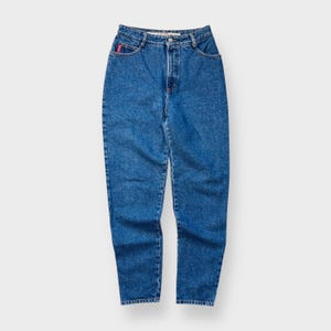 Puede incluir: Vaqueros de mezclilla azules con cintura alta y pernera recta. Los vaqueros tienen un diseño clásico de cinco bolsillos, cierre de botón y cremallera, y un pequeño logotipo rojo en el bolsillo delantero.