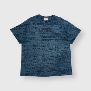 Op de afbeelding: Blauw T-shirt met ronde hals en korte mouwen, bedekt met een donkerblauw patroon van computercode. Er staat een klein logo op de bovenrug. De stof lijkt een zachte katoenmix te zijn. Casual stijl.
