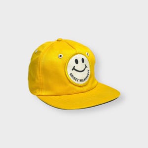 May include: A yellow baseball cap with a black and white smiley face patch that says "Grisez Warehouse" on it.