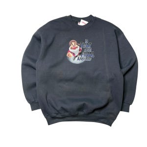 Op de afbeelding: Donkergrijze sweatshirt met een afbeelding van een Disney-personage en de tekst "IS THAT YOUR FINAL ANSWER?". De afbeelding toont een stripfiguur in een rode jas en witte baard. De sweatshirt heeft een ronde hals en lange mouwen.