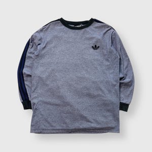 May include: Gray long-sleeve shirt with black trim and the Adidas trefoil logo. The left sleeve has three navy blue stripes. The shirt has a crew neck and black cuffs.