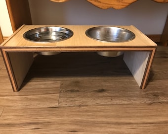 May include: A wooden elevated dog bowl stand with two stainless steel bowls. The stand is made of light wood with a natural finish.