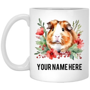 May include: White ceramic mug with a watercolor illustration of a guinea pig surrounded by red flowers and green leaves. The text "YOUR NAME HERE" is printed in black at the bottom of the mug.