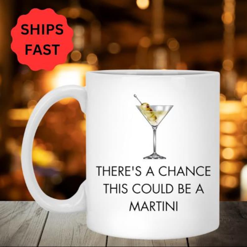 K&ouml;nnte beinhalten: Eine wei&szlig;e Keramiktasse mit schwarzem Henkel. Die Tasse zeigt ein Motiv eines Martini-Glases mit einer Olive und dem Text "There's a chance this could be a martini".