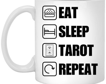 May include: White ceramic coffee mug with black text that reads "Eat Sleep Tarot Repeat" with icons for a hamburger, bed, tarot cards, and a circular arrow.