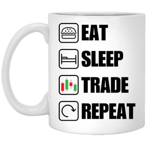 May include: White ceramic mug with a black and white graphic that reads "Eat Sleep Trade Repeat" with icons for a hamburger, bed, a candlestick chart, and a circular arrow.