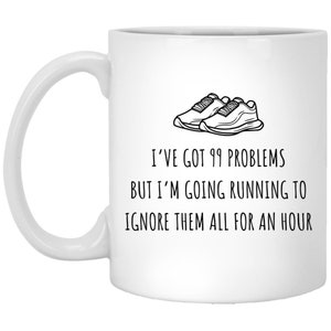 以下が含まれることがあります： 白地に黒と白のランニングシューズのイラストと「99の問題を抱えているけど、1時間走って全部無視する」というテキストが書かれた白いセラミック製のコーヒーカップ