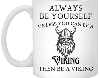 May include: White ceramic mug with a black Viking graphic and the text "ALWAYS BE YOURSELF UNLESS YOU CAN BE A VIKING THEN BE A VIKING". The mug has a curved handle.