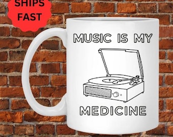 May include: White ceramic mug with a black outline of a record player and the text "Music is my medicine".