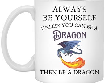 Puede incluir: Taza de cerámica blanca con el texto "ALWAYS BE YOURSELF UNLESS YOU CAN BE A DRAGON THEN BE A DRAGON". La taza presenta una ilustración de un dragón azul que escupe fuego. Un regalo divertido para los amantes de la fantasía.