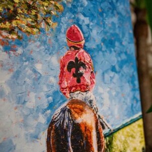 May include: Oil painting of a jockey on a horse, viewed from behind. The jockey wears a red cap and jacket with a black fleur-de-lis. The background features a blue sky and green grass, with a tree in the upper left corner.