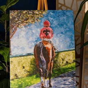 May include: An oil painting on canvas depicts a jockey on a brown horse, viewed from behind. The jockey wears a red jacket with a black emblem and a red cap. The background shows a blue sky, a green field, and a tree.