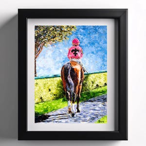 May include: Framed artwork depicting a horse and jockey on a racetrack. The jockey wears a pink uniform with a black emblem. The horse is brown with a white-stockinged leg. The background features a blue sky, green grass, and a tree.